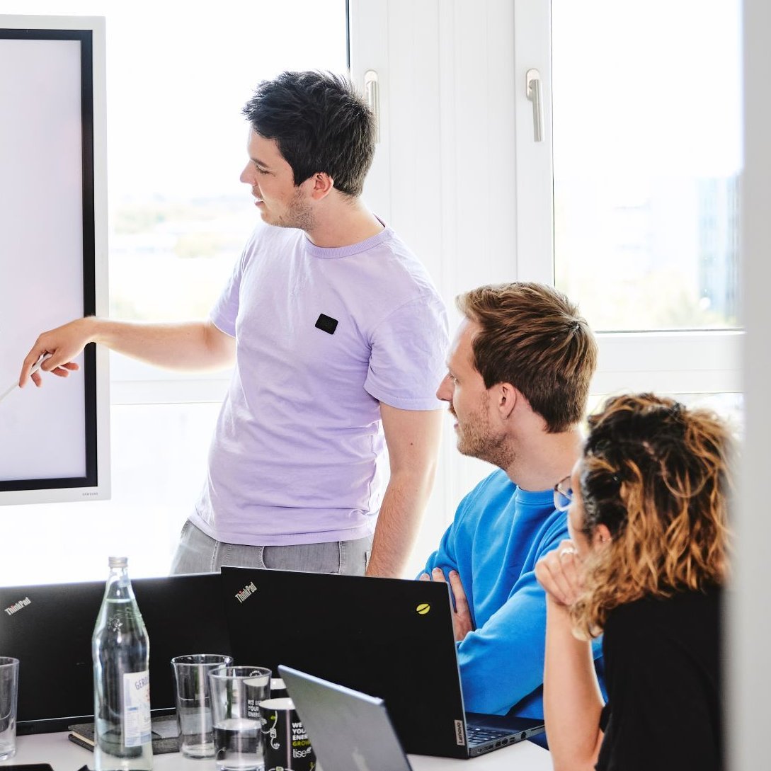 Ein lise-Entwickler zeigt anderen Mitarbeitern auf einem Whiteboard, wie mit KI Probleme gelöst werden können 