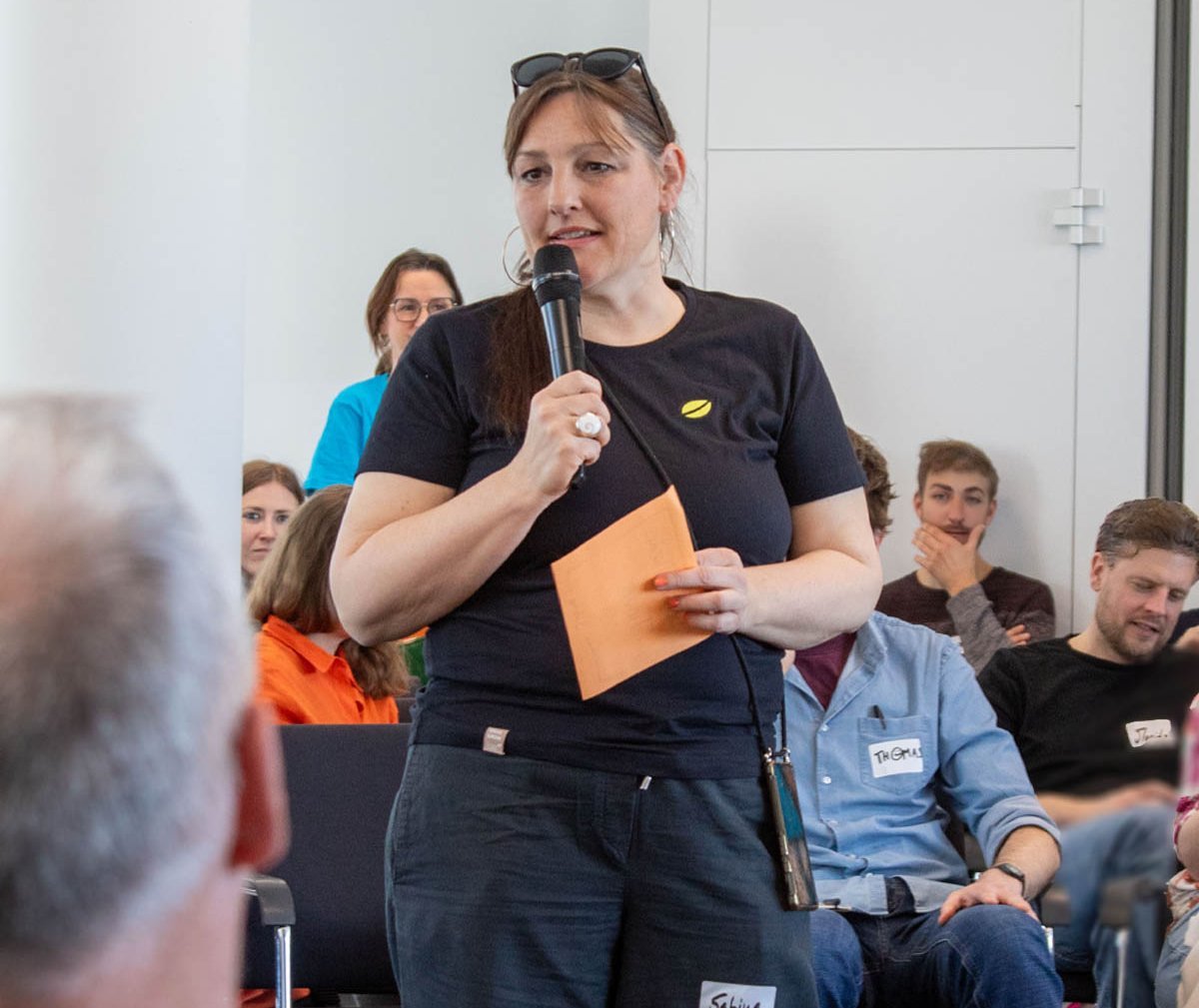 Beim Treffen der agilen Agilisten spricht eine lise-Mitarbeiterin in ein Mikrofon und hält orangene Notizzettel in der Hand