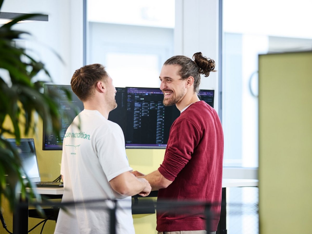 Zwei lise-Entwickler stehen vor einem Computer und schauen sich lachend an