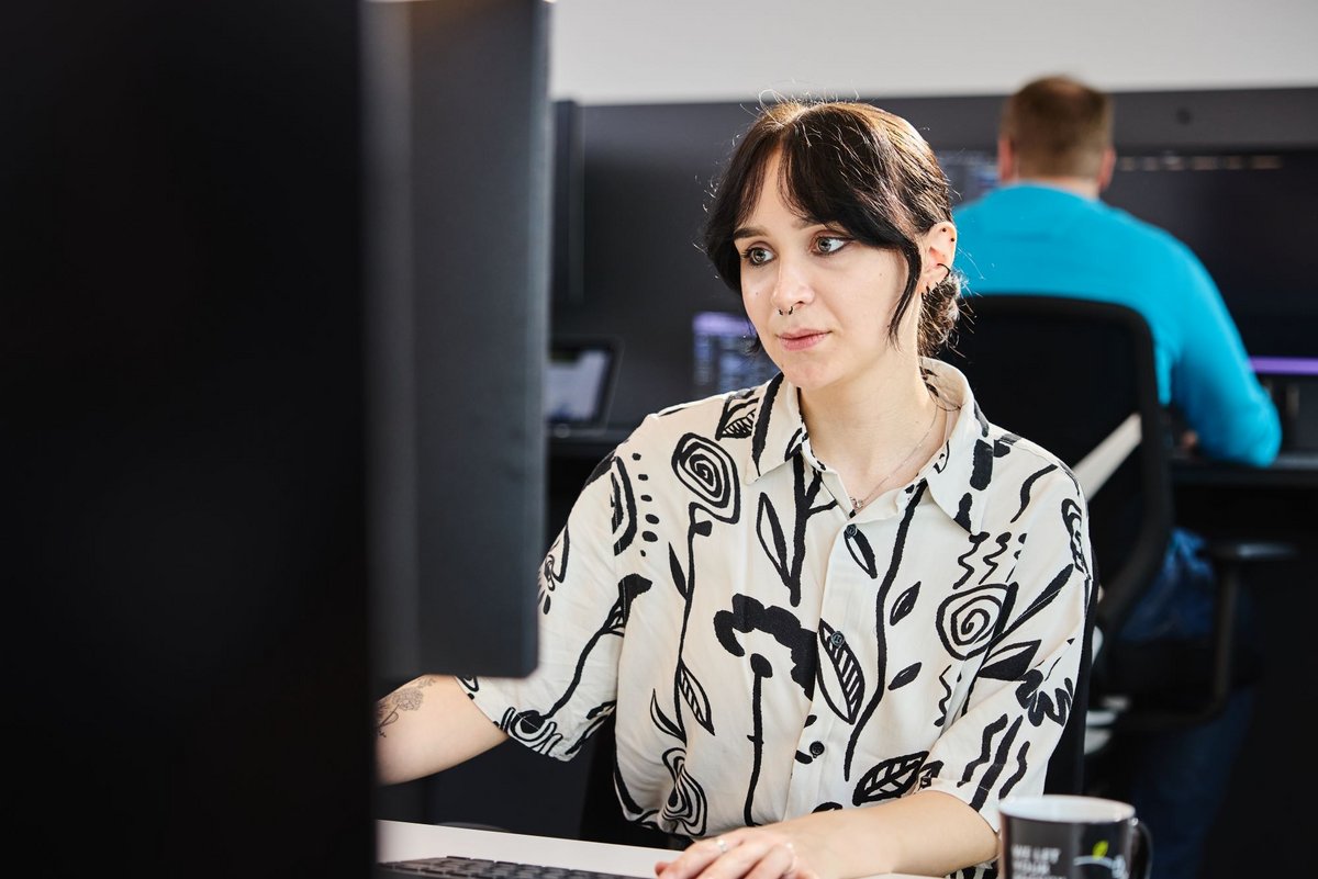 Eine lise-Entwicklerin mit einer weißen Bluse mit schwarzen Mustern wartet eine Software auf dem Computer