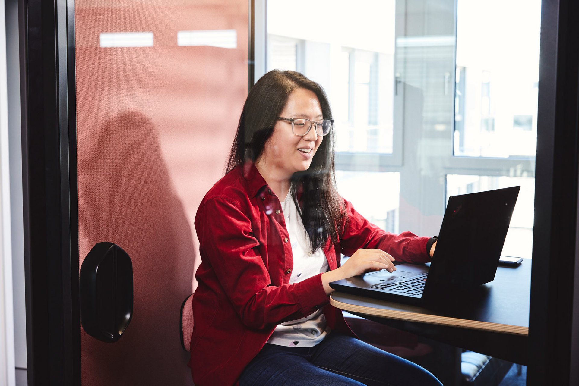 lise Kollegin sitzt in einer Büro-Telefonzelle am Laptop. 