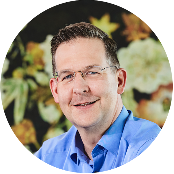 Foto von Dr. Tobias Krautkremer, einer der Geschäftsführer, in einem blauen Hemd vor einem bunten Hintergrund