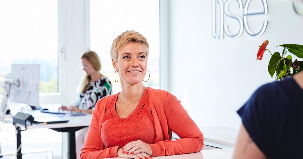 Eine lise-Mitarbeiterin in einem roten Outfit unterhält sich offen mit einem Mitarbeiter in den lise-Räumlichkeiten